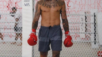 Tattooed male MMA fighter wearing grey shorts and red boxing gloves inside a training cage